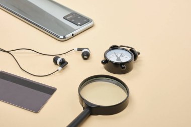 İnternetten alışveriş konsepti. Kredi kartı kulaklıklı akıllı telefon, büyüteç, bej arka planda çalar saat.