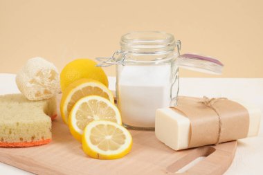 Temizlik için çevre dostu temizlik seti, soda ve limon, sıfır atık yaşam tarzı konsepti. Cam kavanozda kabartma tozu, sabun, luffa ve bej arka planda dilimlenmiş limon.
