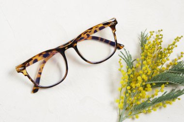 Modern gözlük ve bej ışıklı arka plan fotokopi alanı, yaz ve bahar ruh hali konsepti üst görünüm üzerine mimoza dalı.