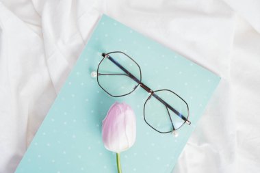 Bardaklar, not defterleri ve lale çiçekleri beyaz kumaş, bahar havası konsepti, bahar sabahını yatağın üstünde geçir.