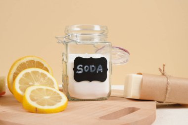 Temizlik için çevre dostu temizlik seti, soda ve limon, sıfır atık yaşam tarzı konsepti. Cam kavanozda kabartma tozu, sabun, luffa ve bej arka planda dilimlenmiş limon.