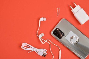 Metal gövdeli ve akıllı telefon bileşenli modern akıllı telefon kırmızı arka plan fotokopi alanı, şarj ipuçları vs. aksesuarlar