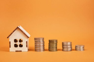 Küçük ahşap ev modeli ve kahverengi arkaplan satışı ve emlak konsepti, inşaat veya ev kirası üzerine çok sayıda madeni para kuleleri