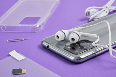 Mor arka planda bir akıllı telefon için aksesuarlar, koruyucu cam, kasa, kulaklık, şarj aleti ve diğer aksesuarlar.