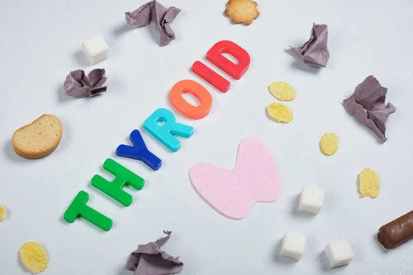 wads of paper, sweets, felt thyroid gland and the inscription thyroid gland on a gray background,, treatment of thyroid diseases with the help of diet concept, junk food
