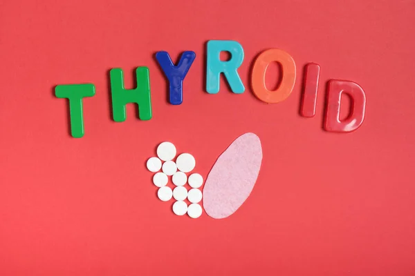 silhouette of the thyroid gland from pills and pink felt and the inscription thyroid on a red background top view copy space