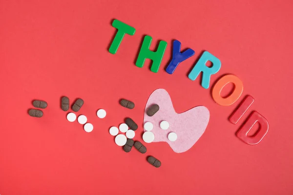 silhouette of the thyroid gland from pink felt, pills and the inscription thyroid gland on a red background top view