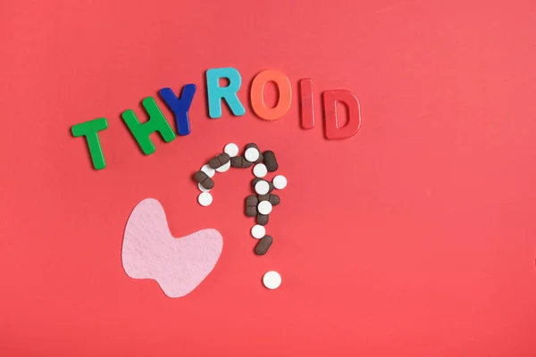 silhouette of the thyroid gland from pink felt, a question mark from pills and the inscription thyroid gland on a red background top view copy space