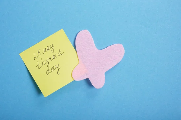 thyroid gland from pink felt and a yellow sticker with the inscription thyroid gland day 25 may on a blue background, diagnosis and treatment of thyroid disease concept