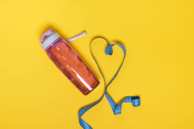 Yeniden kullanılabilir plastik su şişesi ve sarı arka plan üst görünüm kopyalama alanı üzerindeki mavi ölçüm bandı