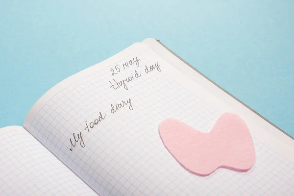 notepad, and silhouette of the thyroid gland cut out of pink felt on a blue background, nutrition for diseases of the thyroid gland concept copy space