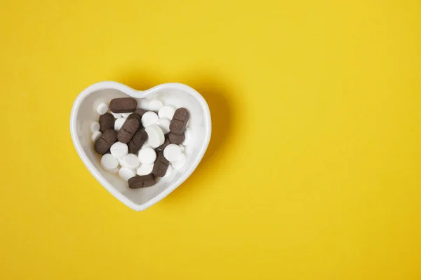 Pílulas Brancas Marrons Uma Pequena Placa Forma Coração Amarelo Espaço — Fotografia de Stock