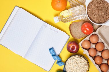 Bir diyet defteri ve sarı arka planda diyet yemeği planlıyorum. Su, mezura ve sağlıklı yiyecekler.