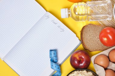 Bir diyet defteri ve sarı arka planda diyet yemeği planlıyorum. Su, mezura ve sağlıklı yiyecekler.