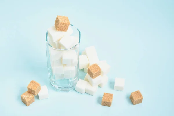 cubes of white and brown sugar in a glass and on a light blue and beige background copy space