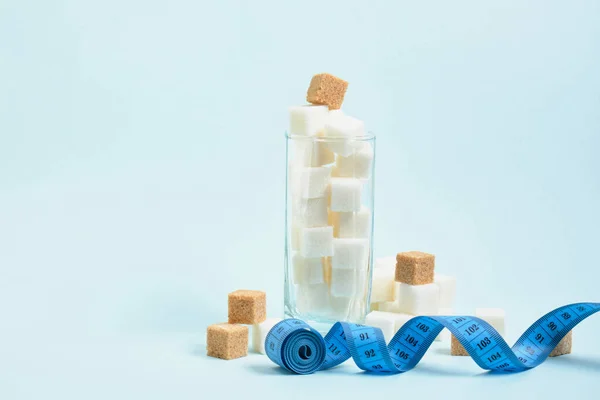 Fita métrica e cubos de açúcar branco e mascavo em um espaço de cópia de vidro, açúcar em bebidas e conceito de comida — Fotografia de Stock