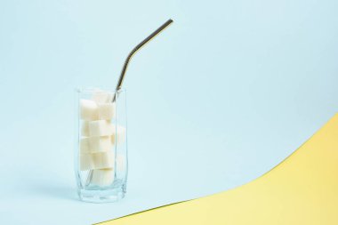 metal yeniden kullanılabilir kokteyl tüpü ve bir bardak beyaz şeker, açık mavi ve sarı arkaplan kopyalama alanı, içeceklerdeki yüksek şeker içeriği ve yiyecek konsepti