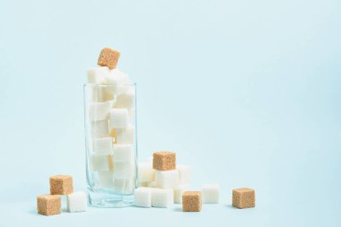 Bardakta beyaz ve esmer şeker küpleri ve açık mavi ve bej arka planda fotokopi alanı, içeceklerde şeker ve yiyecek konsepti.