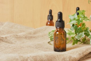 Kahverengi cam şişe damlatıcısı kozmetik yağlı ve keten kumaş üzerine bitki, kahverengi arka plan