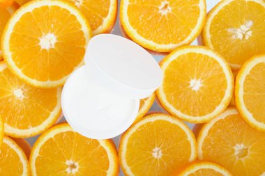 Dilimlenmiş portakal, yüz ve vücut kremi arkaplanında beyaz krema kavanozunu aç. Portakal yağı konseptini de ekle.