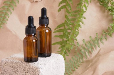 Kahverengi arka planda beton bir blokta kozmetik için pipeti olan iki kahverengi cam şişe. Doğal malzemeler konseptinden kozmetik yağı..