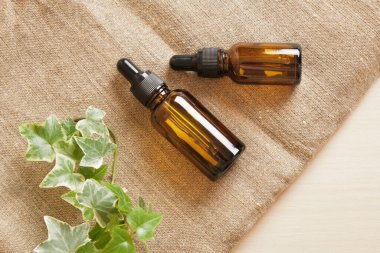 Kahverengi cam şişe damlatıcısı kozmetik yağlı ve keten kumaş üzerine bitki, kahverengi arka plan