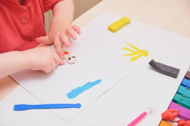 Masanın üzerinde renkli mankenlerle oynayan küçük bir kız. Kil ile ev eğitimi oyunu. Erken gelişim konsepti, çocuk plastikten heykel yapıyor