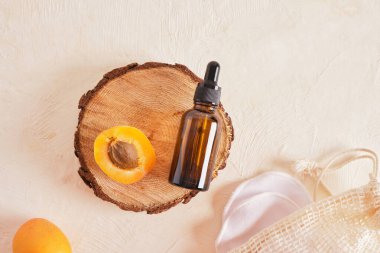 Bej arka plan, yağ veya vücut bakımı için serum gibi kozmetik ürünleri içeren kayısılar ve cam kahverengi bir şişe.