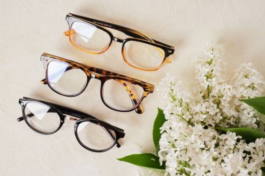 Bir kaç farklı gözlük ve bej arkaplan, gözlük ve çiçek desenli beyaz leylak dalı yer kopyalayabilir.