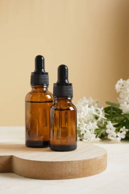 Kozmetik yağlar veya serumlar için kahverengi bir şişe ve bej arka planda beyaz leylak bir dal, vücut ve yüz bakımı için doğal kozmetik..
