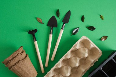 Yeşil arka planda bahçe aletleri. Tohum ekmek için küçük kürekler ve tırmıklar ve kapalı bitkiler, çevre dostu bahçe konsepti