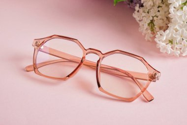 Son moda gözlük ve pembe arka planda beyaz leylak dalı, gözlük ve çiçekler, şeffaf renkli gözlük çerçevesi.