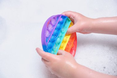 Çocuğun elinde silikon köpüklü anti-stres oyuncağı var. Banyoda sabunlu köpüğe koyuyor.