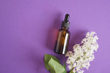 Kozmetik yağlar veya serumlar için kahverengi bir şişe ve parlak mor arka planda beyaz leylak yüz ve vücut bakımı için doğal kozmetik ürünler. Boşluk üst görünümünü kopyala