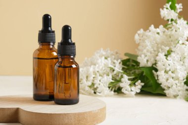 Kozmetik yağlar veya serumlar için kahverengi bir şişe ve bej arka planda beyaz leylak bir dal, vücut ve yüz bakımı için doğal kozmetik..