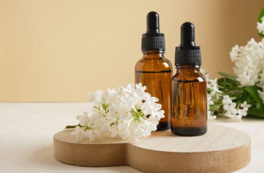 Kozmetik yağlar veya serumlar için damlatan kahverengi bir şişe ve bej arka planda beyaz leylak dalı.