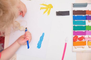 Masanın üzerinde renkli mankenlerle oynayan küçük bir kız. Kil ile ev eğitimi oyunu. Erken gelişim konsepti, çocuk plastikten heykel yapıyor