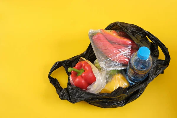 black plastic bag with groceries on yellow background copy space say no to plastic concept