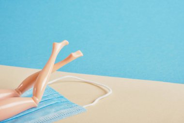 Bebek bacakları mavi ve bej bir arka planda mavi bir maskenin üzerinde yatıyor. Coronavirüs salgını sırasında plaj tatili ve tuzizm. Virüsten korunma.