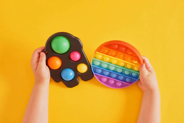 Juguetes coloridos simple hoyuelo y pop en manos de los niños sobre un fondo amarillo —  Fotos de Stock