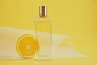 Limon kokusu, limon kokulu parfüm, limon dilimi ve sarı arka planda bir şişe parfüm.