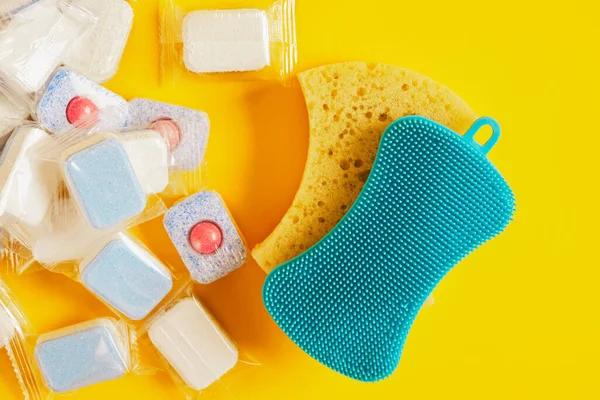 dishwasher tablets and two different eco scrubbing sponges on a yellow background, dishwashing products, hand wash the dishes or use the dishwasher