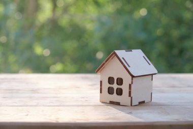 Ahşap masadaki küçük ev modeli, doğa yeşil bokeh soyut arka plan. Aile hayatı ve iş yeri konsepti.