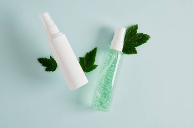 Kozmetik ürünleri için iki farklı pompa klasik şişesi, kozmetik kaplar ve açık mavi arka planda taze ağaç yaprakları, jöleli şeffaf bir şişe ve logolu beyaz bir şişe, üst görünüm taklit