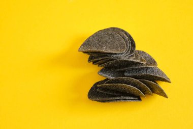 Sarı arka planda siyah patates cipsi. Tuzlu siyah cips, aktif kömür ve kırmızı biber..