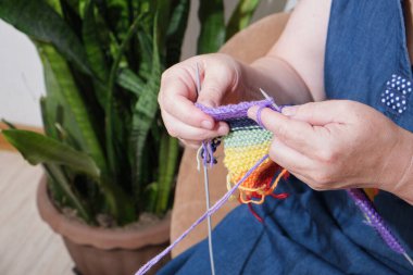 Yetişkin bir kadın, Igbt topluluğunun bayrağını örüyor. Koltuğunda oturan eşcinsel gururunun sembolü. Gökkuşağı. Doku. Yakın plan..
