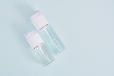 Açık mavi arka planda beyaz kapaklı iki boş cam şişe, kozmetik şişeler, jel ve parfümlü şişe üst görünümde fotokopi alanı.