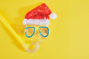 Dalış seti, Noel Baba şapkası, güneş kremi ve sarı arka planda bir şişe limonata, sıcak bir ülkede Noel tatilleri