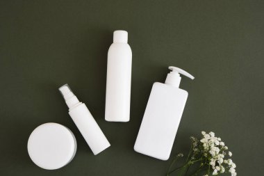 Alüminyum kozmetik kavanozu ve koyu yeşil arka planda üç farklı beyaz şişe, kozmetik ürünleri doğal kozmetik ambalajlarını taklit ediyor. Güzellik ürünleri konsepti.