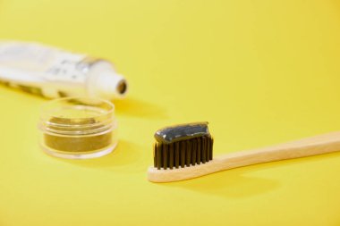 Siyah kömür diş macunlu bambu diş fırçası kömür sarısı arkaplan tüpü ve kömür kömürü siyah macunu dolu kavanoz.
